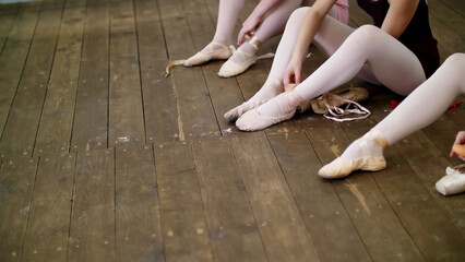 close up, ballerinas change their shoes into special ballet shoes, pointe shoes, lace with ballet ribbons, on an old wooden floor, in ballet class. High quality photo