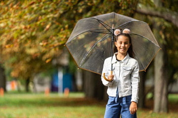 Little child walking with umbrella in the rain in fall park