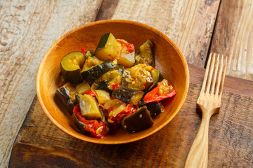 A plate of grilled vegetables on a wooden board next to a wooden fork.