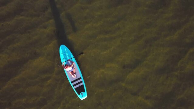 A woman on a SUP board in a mohawk swimsuit floats on the water aerial video. Top view general plan.