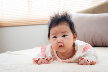 close-up of Newborn 3 month old Asian woman playing in bed in the bedroom of the house. After waking up, he looked for his mother in frustration, lowering his head and raising his head.