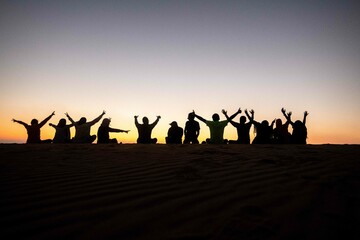 A group of people, team work, companions, friends sitting together during sunrise or sunset,...