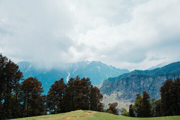 Fototapeta na wymiar View of Dhauladhar mountain range covered with clouds as seen from Bhrigu lake trek in Manali, Himachal Pradesh, India. Mountain range of the Middle Himalayas. Indian Himalayas.