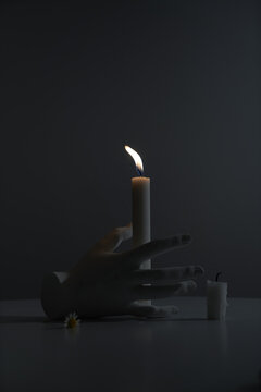 A candle on a dark background next to an artificial hand on the table
