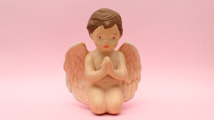 Figura de ceramica de angel orando incado sobre un fondo rosa claro. 
