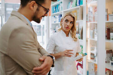 Fototapeta na wymiar Young business man choosing and buying drugs in a drugstore while talking with attractive female pharmacist. She helping him with expert advice.
