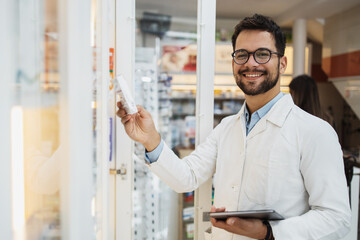 Young male pharmacist working in a drugstore. He is happy and smiled.