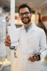 Young male pharmacist working in a drugstore. He is happy and smiled.