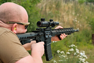 a man is holding an automatic weapon. a man looks into the sight of a military weapon.