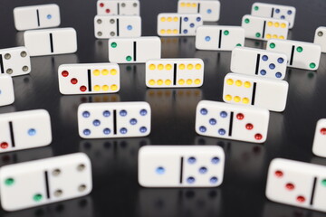 White domino pieces with colored dots over a black wood table