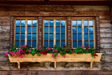 traditional wooden window with flowers alp lodge Switzerland with mountains reflection on glass.