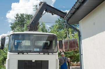 Unloading paving slabs from a truck. Men unload paving slabs using a manipulator. Workers unload building materials from a large machine.