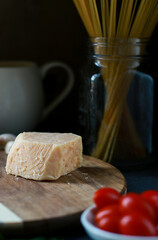 close up of parmesan cheese on wooden board with tomatoes, basil, pasta and grater