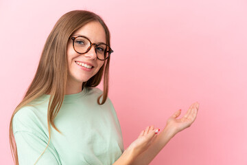 Young Lithuanian woman isolated on pink background With glasses and presenting something