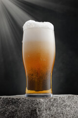 Draught beer in glass on a granite stone. Glass of fresh and cold beer on gray dark background. Selective focus