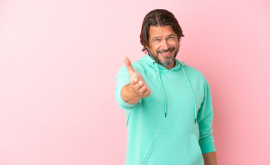 Senior dutch man isolated on pink background shaking hands for closing a good deal