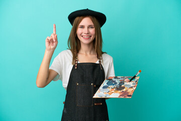 Young artist English woman holding a palette isolated on blue background pointing up a great idea