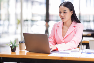 Fototapeta premium Asian Businesswoman Using a laptop computer and working at office with calculator document on desk, doing planning analyzing the financial report, business plan investment, finance analysis concept.