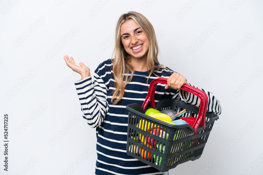 Canvas Prints Young caucasian woman holding a shopping basket full of food isolated on white background extending hands to the side for inviting to come