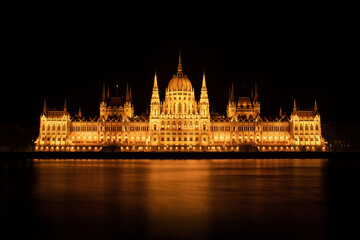 Fototapeta na wymiar Hungarian Parliament Building or Országház in front of the Danube river at night. Beautiful night landscape with an illuminated monument. Summer landscape scene from the city of Budapest, Hungary