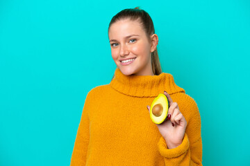 Young caucasian woman holding an avocado isolated on blue background smiling a lot