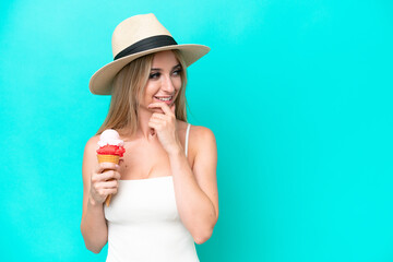 Blonde woman in swimsuit holding an ice cream isolated on blue background thinking an idea and looking side