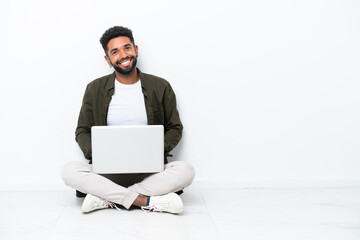Young Brazilian man with a laptop sitting on the floor isolated on white posing with arms at hip and smiling
