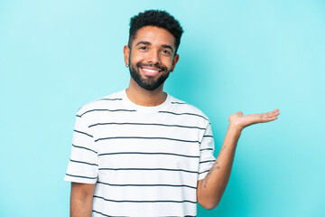 Young Brazilian man isolated on blue background holding copyspace imaginary on the palm to insert...