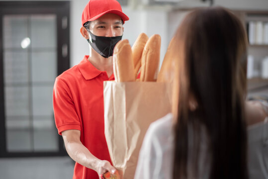Young Asian Woman Picked Up The Bread Package From Delivery Man Rider Ware Red Uniform With Smile Feeling Happy. Online Shopping And Food Delivery Concept