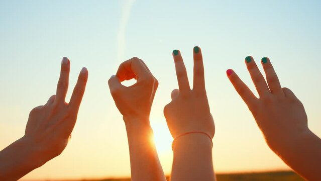 Signs symbols with four human hands against blue sky. Two,three fingers. Arm in form circle. Gestures. Friendship teamwork. Close up group raising hands up. Sunny day in summer nature outdoor.