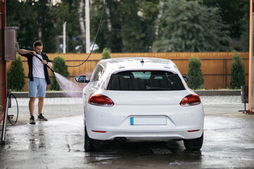 Man washing white car at contactless self-service car wash. Washing sedan car with foam and...