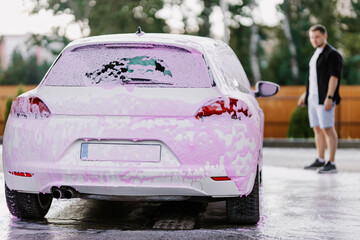 White sedan in pink soapy foam. Contactless self-service car wash. Personal car care cleaning...