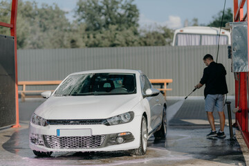Man washing white car at contactless self-service car wash. Washing sedan car with foam and...