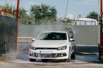 Man washing white car at contactless self-service car wash. Washing sedan car with foam and...