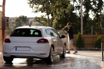Man washing white car at contactless self-service car wash. Washing sedan car with foam and...