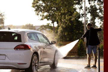 Man washing white car at contactless self-service car wash. Washing sedan car with foam and...