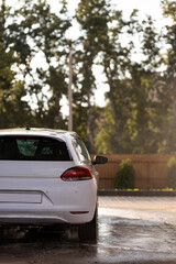 White car sedan at contactless self-service car wash at sunset. Personal car care cleaning outside...