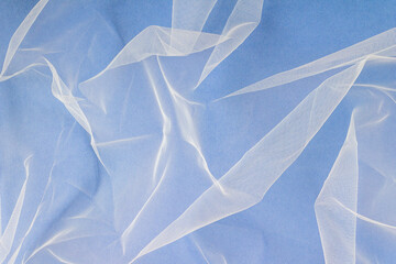 sheer tulle fabric arranged in soft folds on a blue background, selective focus