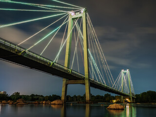Cable-stayed bridge across the river at night. Night illumination of buildings, reflections.