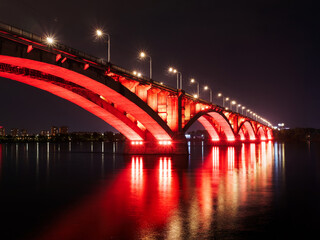 Fototapeta na wymiar Arch bridge across the river at night. Night illumination of buildings, reflections.