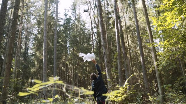 Lost thin young man actively waves white rag to attract the attention of rescuers. Drone of the rescue service flies over the man. The concept of technologies for rescuing lost people in the forest.
