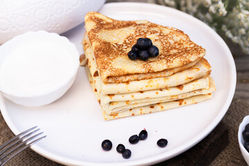 pancakes are placed in a triangle with blueberries on a white plate laid on a wooden background