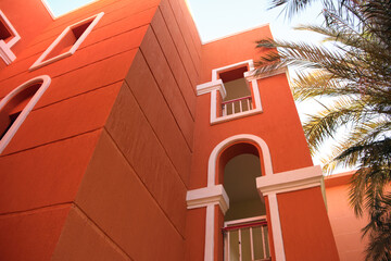 Fragment of red brick resort hotel exterior with palm trees under blue summer sky