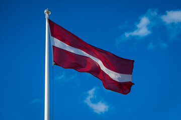 Latvian flag waving in wind. Flag of Latvia on blue  sky background. 