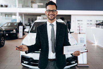 Good looking, cheerful and friendly salesman poses in a car salon or showroom.