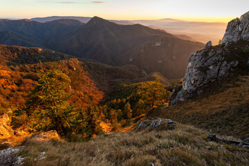 Landscape scenery in mountains at sunset in autumn. Sun setting behind a rock on top of the slope. Horizontal wide angle view of nature in fall golden colors.