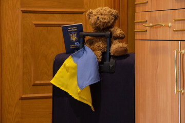 A suitcase with a teddy bear flag of Ukraine and a biometric foreign passport of Ukraine stands in the corridor at the exit from the house, Ukrainian