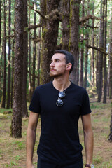 Retrato hombre blanco con camiseta negra y gafas de sol en el bosque