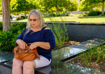 Mature white woman sitting on a city park searching for an item in her purse