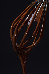 Chocolate is whipped with a whisk. Close-up of a wire whisk and melted chocolate on a black...